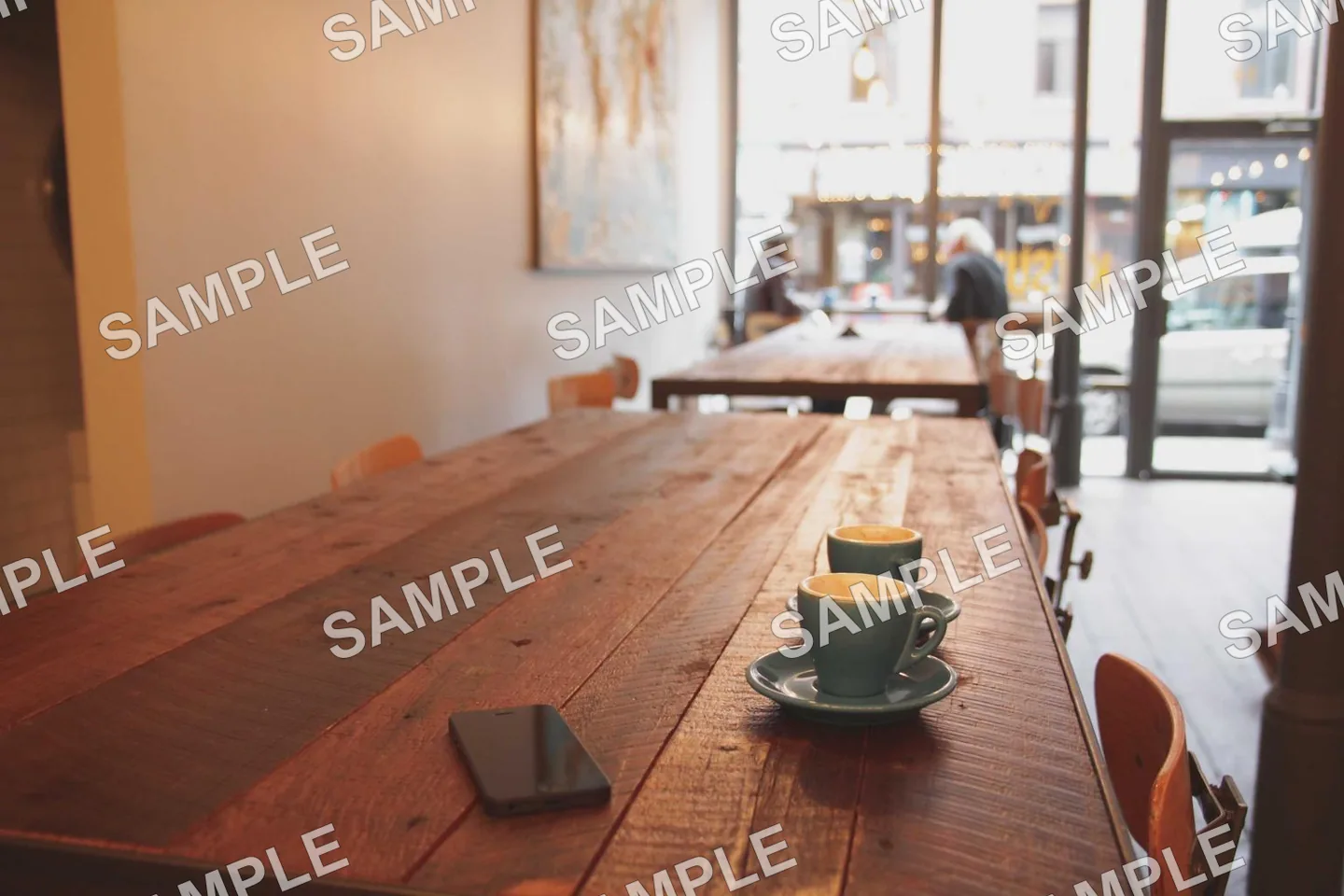 Sunlit cafe interior with a long wooden table, covered by a repeating SAMPLE watermark grid